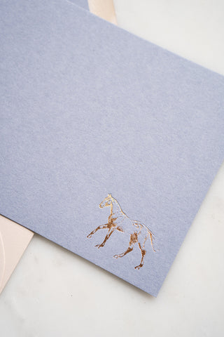 Photo of a lavender correspondence card with a gold foil stamped design featuring a drawing of a horse cantering by equine artist Danielle Demers.