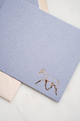 Photo of a lavender correspondence card with a gold foil stamped design featuring a drawing of a horse trotting by equine artist Danielle Demers.