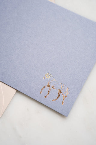 Photo of a lavender correspondence card with a gold foil stamped design featuring a drawing of a horse trotting by equine artist Danielle Demers.