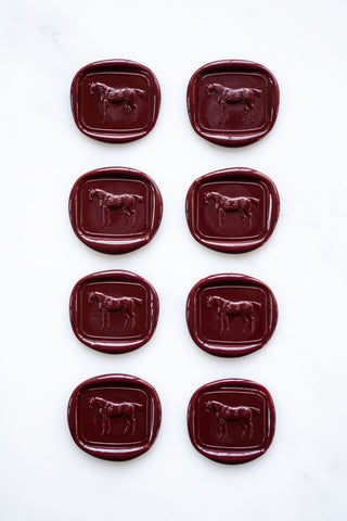 Photo of a set of eight deep burgundy wax seals featuring a three-dimensional intaglio impression of a horse designed by equine artist Danielle Demers