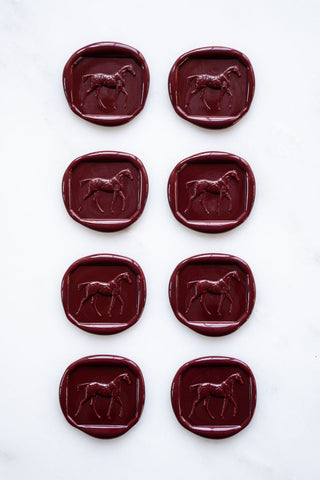 Photo of a set of eight deep burgundy wax seals featuring a three-dimensional intaglio impression of a horse designed by equine artist Danielle Demers