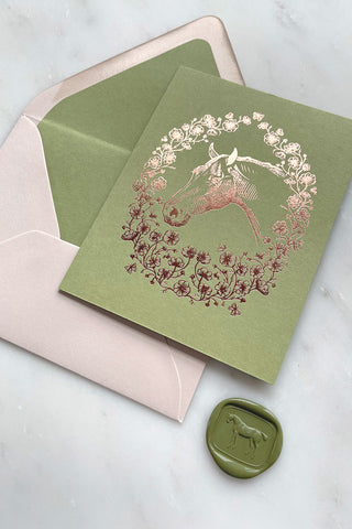 Photo of a rich copper metallic foil stamped note card, featuring a drawing of a horse in a wreath of cosmos flowers, bees and butterflies, on spring green 111lb card stock by equine artist Danielle Demers.