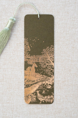 A foil stamped bookmark featuring a countryside autumn scene with a horse, fox, pumpkins, pheasant, and crow. Printed in copper foil on a mossy green card stock and finished with a light celadon green tassel.