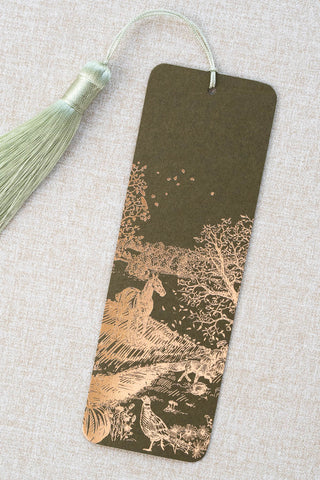 A foil stamped bookmark featuring a countryside autumn scene with a horse, fox, pumpkins, pheasant, and crow. Printed in copper foil on a mossy green card stock and finished with a light celadon green tassel.