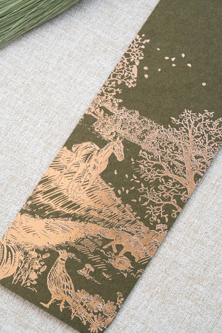 A foil stamped bookmark featuring a countryside autumn scene with a horse, fox, pumpkins, pheasant, and crow. Printed in copper foil on a mossy green card stock and finished with a light celadon green tassel.