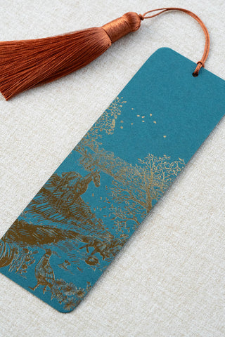 A foil stamped bookmark featuring a countryside autumn scene with a horse, fox, pumpkins, pheasant, and crow. Printed in bronze foil on a dark teal card stock and finished with a deep orange tassel.