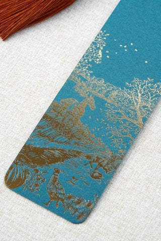 A foil stamped bookmark featuring a countryside autumn scene with a horse, fox, pumpkins, pheasant, and crow. Printed in bronze foil on a dark teal card stock and finished with a deep orange tassel.