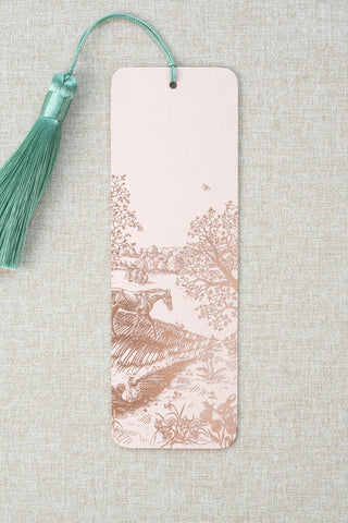 A foil stamped bookmark featuring a countryside spring scene with a horse, swan, rabbits, butterflies and flowers. Printed in rose gold foil on a light peach pink card stock and finished with a light turquoise tassel.