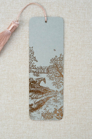 A foil stamped bookmark featuring a countryside spring scene with a horse, swan, rabbits, butterflies and flowers. Printed in bronze foil on a sage green card stock and finished with a light warm blush pink tassel.