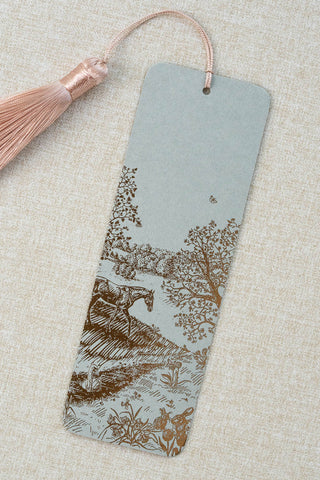 A foil stamped bookmark featuring a countryside spring scene with a horse, swan, rabbits, butterflies and flowers. Printed in bronze foil on a sage green card stock and finished with a light warm blush pink tassel.