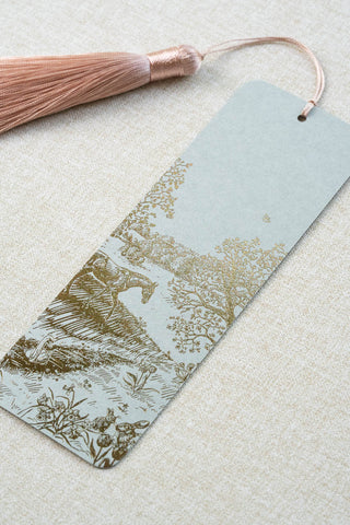 A foil stamped bookmark featuring a countryside spring scene with a horse, swan, rabbits, butterflies and flowers. Printed in bronze foil on a sage green card stock and finished with a light warm blush pink tassel.