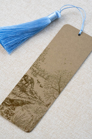 A foil stamped bookmark featuring a countryside summer scene with a horse, flowers, deer, a stoat, birds, butterflies and a bee. Printed in bronze foil on walnut card stock and finished with a sky blue tassel.