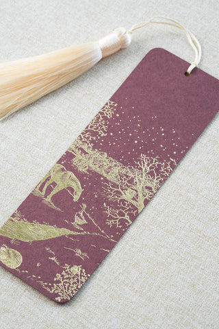 A foil stamped bookmark featuring a countryside winter scene with a horse, goose, hedgehog, robin and red squirrel. Printed in gold foil on a deep maroon card stock and finished with a cream tassel.