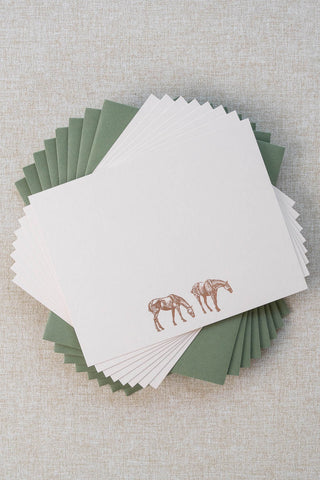 Set of eight cream correspondence cards featuring horse illustrations foil stamped in rose gold. Accompanying medium green envelopes are lined with scalloped-edge dusty blue envelope liners.