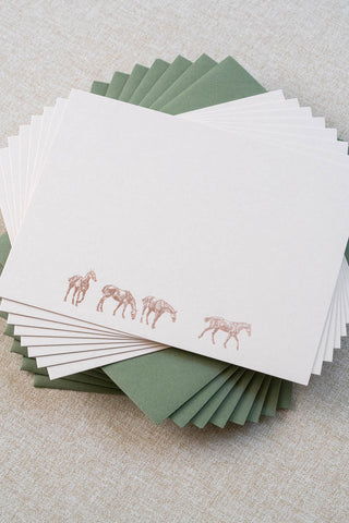 Set of eight cream correspondence cards featuring horse illustrations foil stamped in rose gold. Accompanying medium green envelopes are lined with scalloped-edge dusty blue envelope liners.