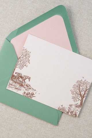 Foil stamped correspondence card featuring a spring scene with a horse, rabbits, tulips, daffodils, trees and butterflies. Rose gold foil design on cream card stock with a green envelope lined in a blush pink liner.