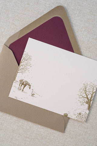 Foil stamped correspondence card featuring a winter scene with a horse, goose, hedgehog, robin, trees and snow. Gold foil design on cream card stock with a taupe envelope lined in a deep cranberry liner.