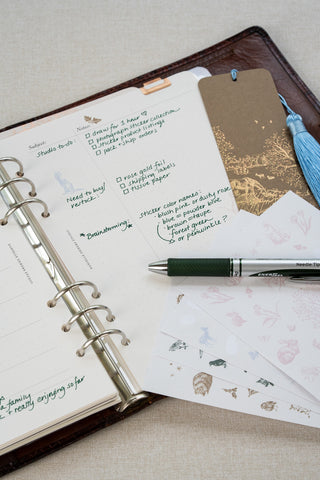 Washi paper stickers used in a Filofax planner page layout. Planner laid open to a two page weekly planner spread. Washi paper sticker sheets featuring delicate illustrations of horses, wildlife and flowers lay over a bottom corner of the planner spread, a foil stamped horse motif bookmark marks the page and a pen sits above.