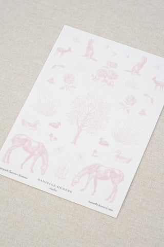 Danielle Demers washi paper sticker sheet on a light beige textured fabric background. The sticker sheet features delicate pink illustrations of horses, countryside animals, and flowers.