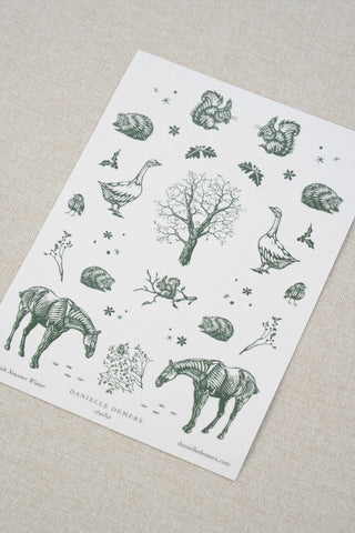 Danielle Demers washi paper sticker sheet on a light beige textured fabric background. The sticker sheet features delicate forest green illustrations of horses, countryside animals, and flowers.