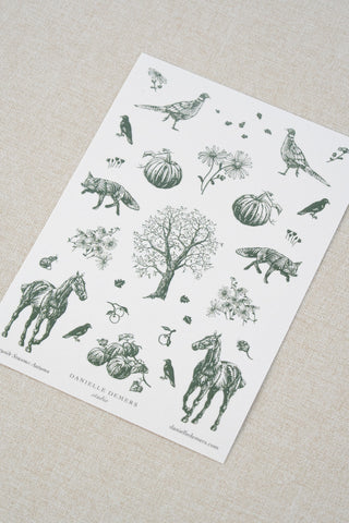 Danielle Demers washi paper sticker sheet on a light beige textured fabric background. The sticker sheet features delicate forest green illustrations of horses, countryside animals, and flowers.