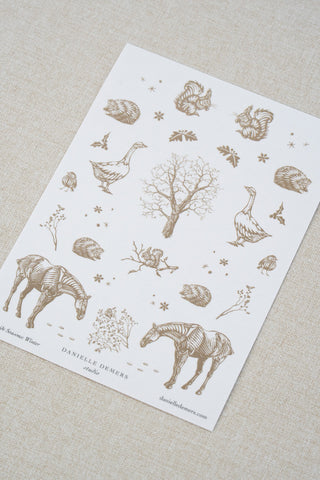 Danielle Demers washi paper sticker sheet on a light beige textured fabric background. The sticker sheet features delicate taupe brown illustrations of horses, countryside animals, and flowers.