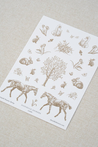 Danielle Demers washi paper sticker sheet on a light beige textured fabric background. The sticker sheet features delicate taupe brown illustrations of horses, countryside animals, and flowers.