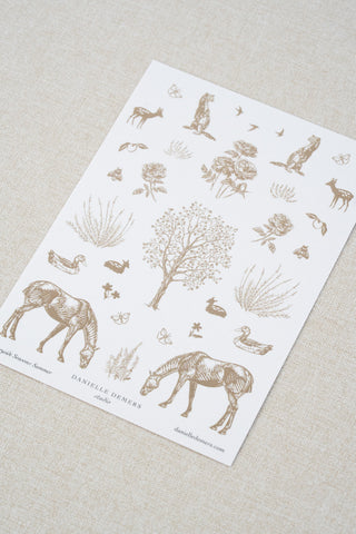Danielle Demers washi paper sticker sheet on a light beige textured fabric background. The sticker sheet features delicate taupe brown illustrations of horses, countryside animals, and flowers.