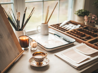 Photo of a drawing table styled with art supplies, candles, a cup of tea and works of art in progress. Photographed in Danielle Demers' studio by Nicole Gearty.