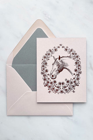 Photo of a rich copper metallic foil stamped design, featuring a drawing of a horse in a wreath of cosmos flowers, bees and butterflies, on cream card stock by equine artist Danielle Demers.