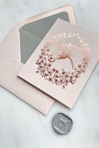Photo of a rich copper metallic foil stamped note card, featuring a drawing of a horse in a wreath of cosmos flowers, bees and butterflies, on cream card stock by equine artist Danielle Demers.